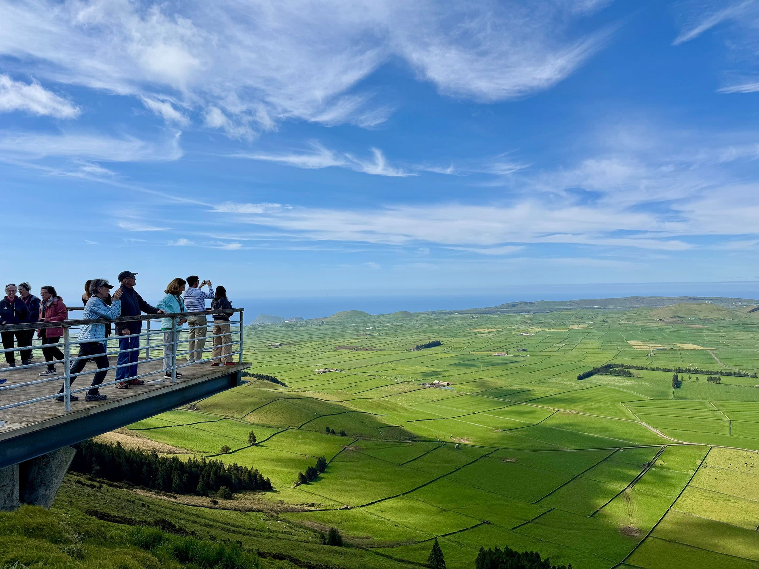 people stand on an observation deck photographing a bright green landscaope