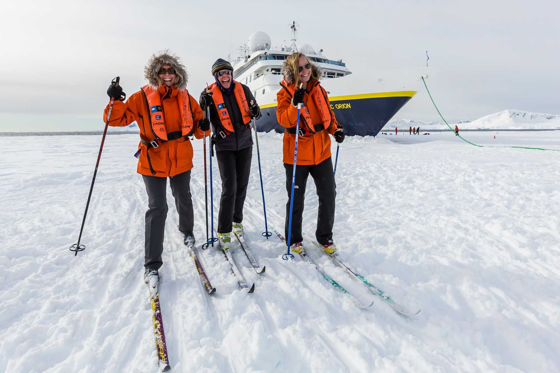 Two women and a man cross-country ski on pack ice in Cape Renaud with the National Geographic Orion parked nearby.