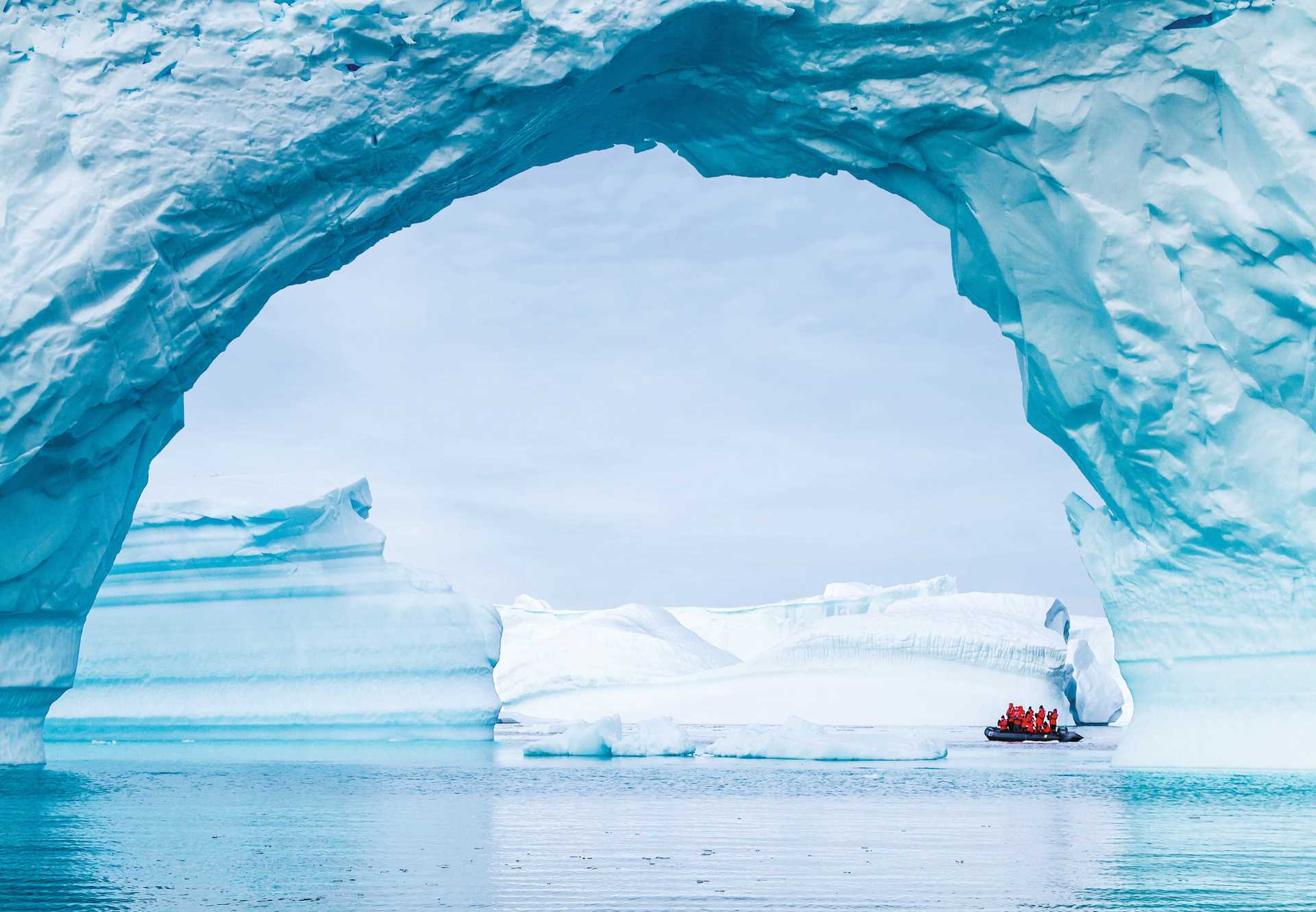 Guests cruise on a Zodiac in the distance under an arch of ice off Booth Island.