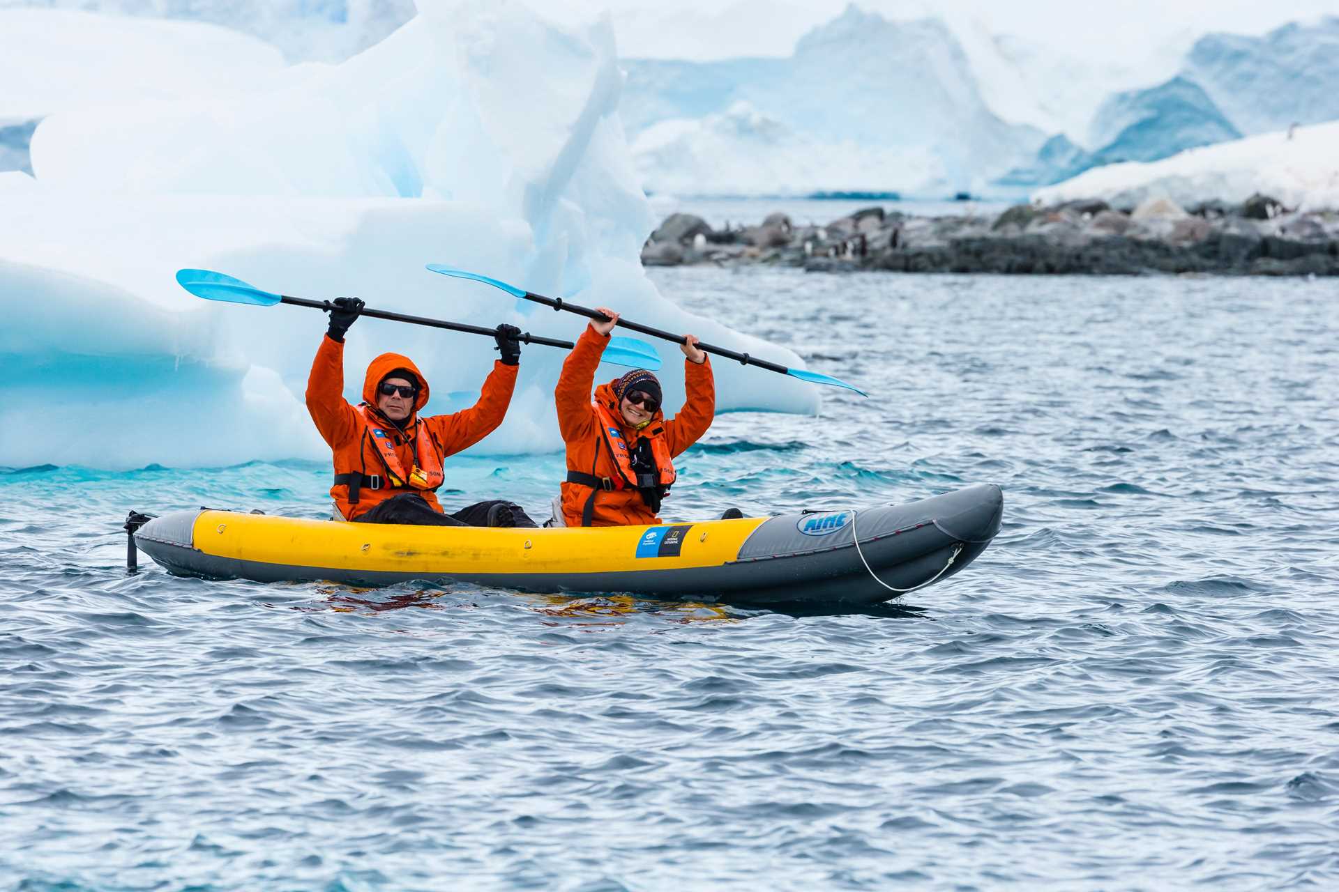 Two kayakers hold their paddles in the air in celebration.