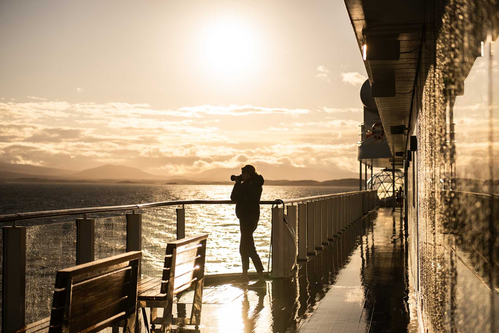 A guest photographs the horizon from the deck of the National Geographic Resolution during golden hour.
