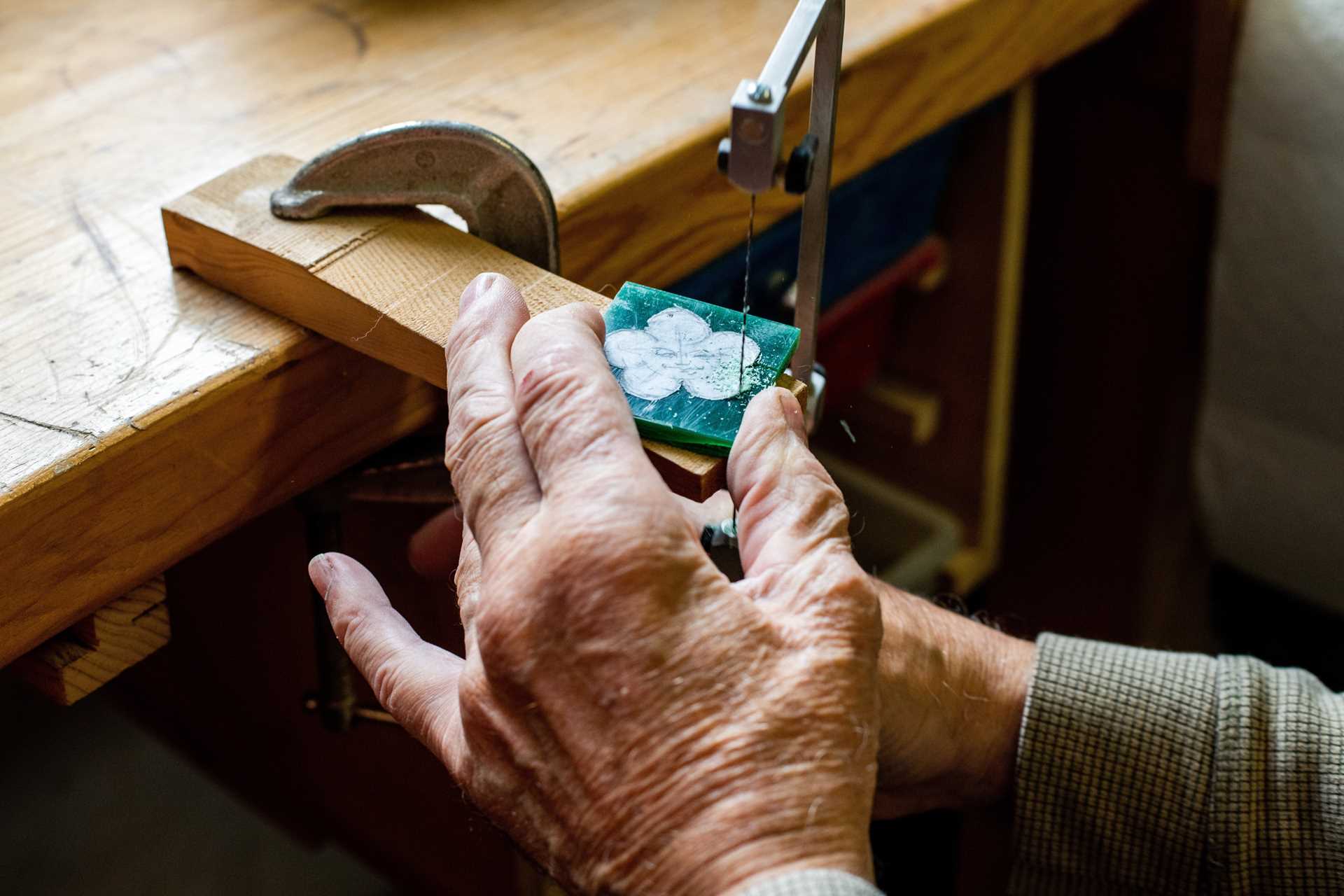 A man carves jewelry on a workbench.