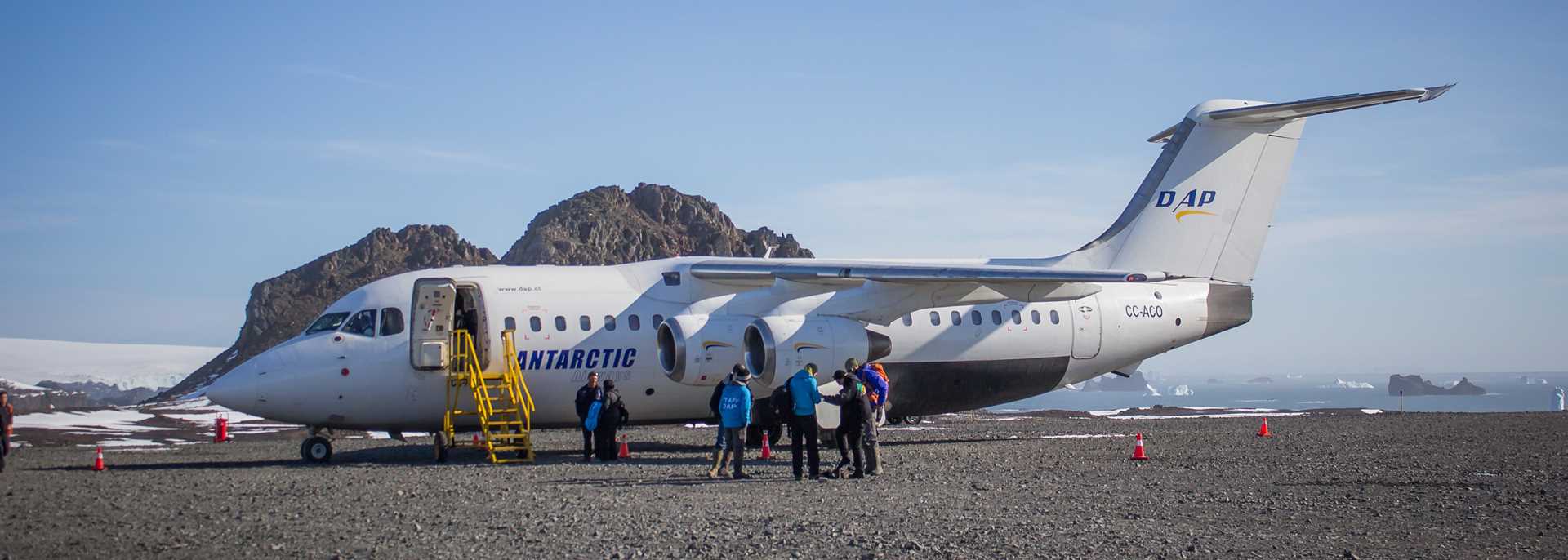 Travelers stand on a tarmac in front of a plane in Antarctica.