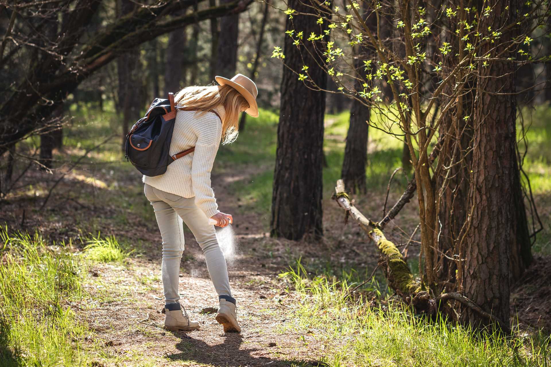 A woman sprays herself with bug spray in the forest.