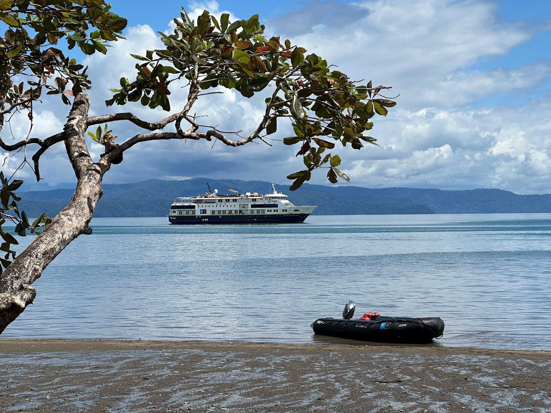 a costa rican beach with a zodiac craft on the shores, with a ship in the background