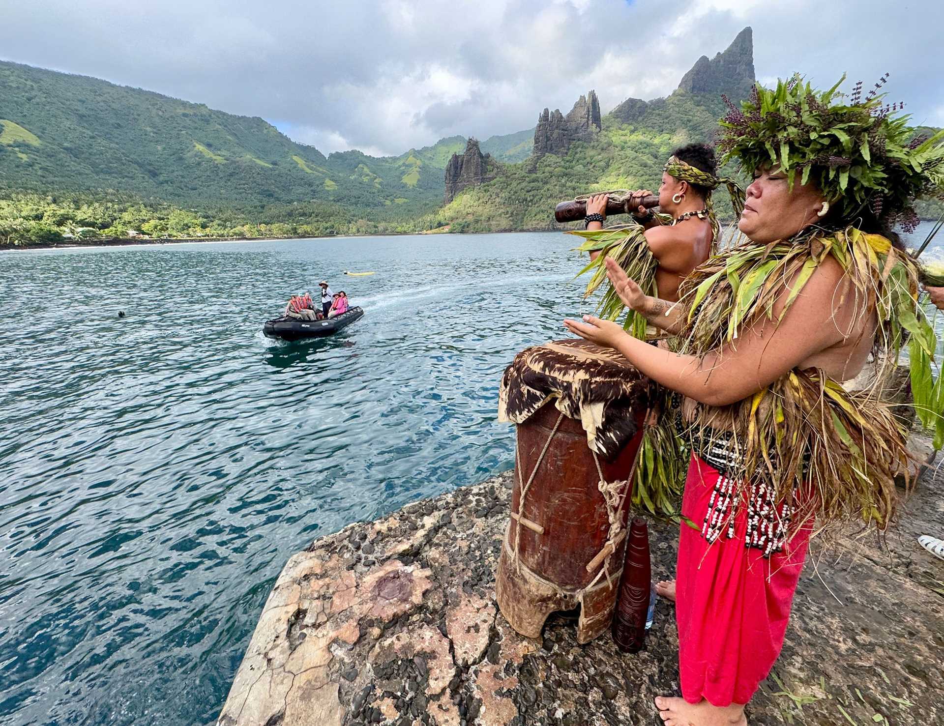 two marquesan islanders in traditional dress watch an approaching ship