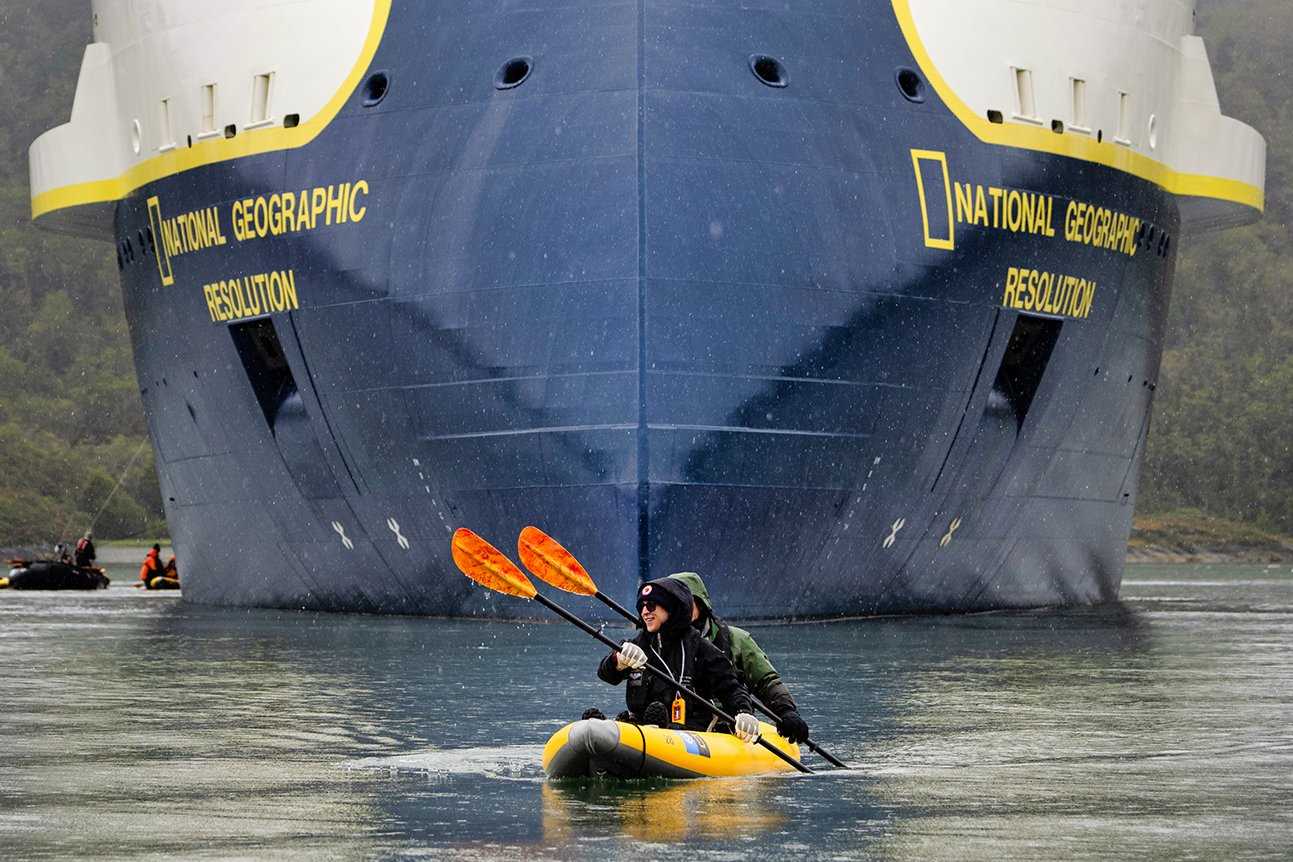 Two guests kayak in front the bow of the National Geographic Resolution in Agostini Fjord, Chile.