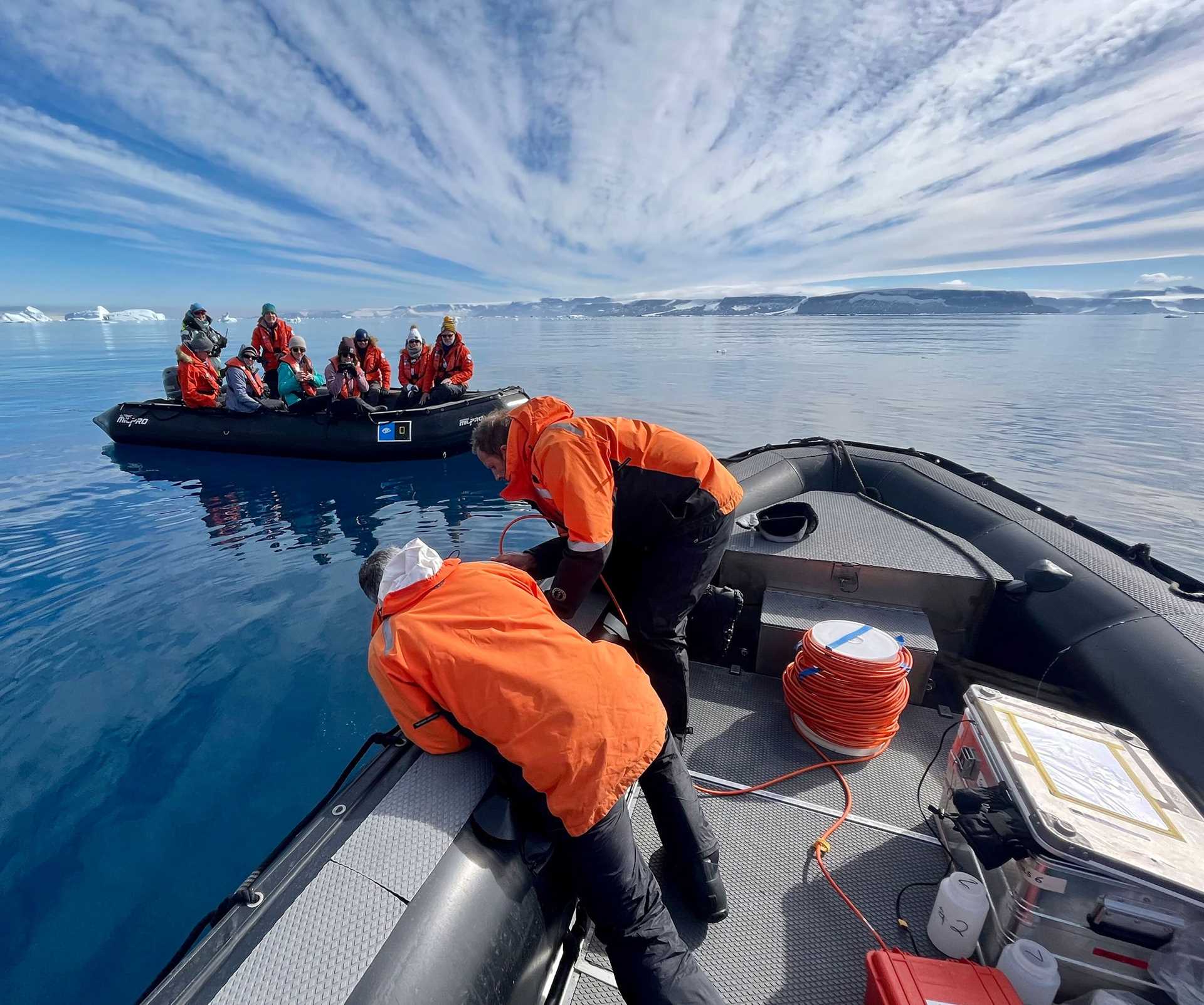 scientists in a zodiac take samples from the water