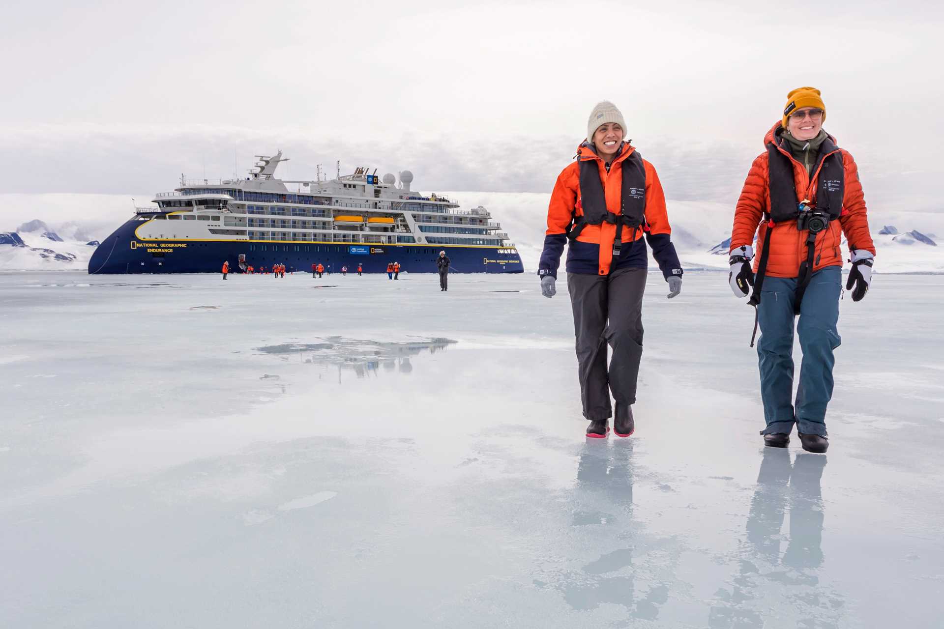 Two women travelers hike on the frozen Weddell Sea with the National Geographic Endurance in the distance.