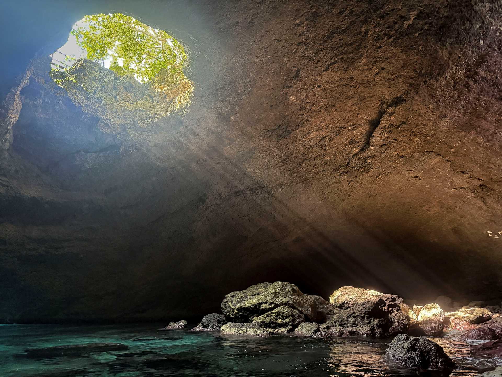 a cave with a large hole near the ceiling casting rays of sunlight