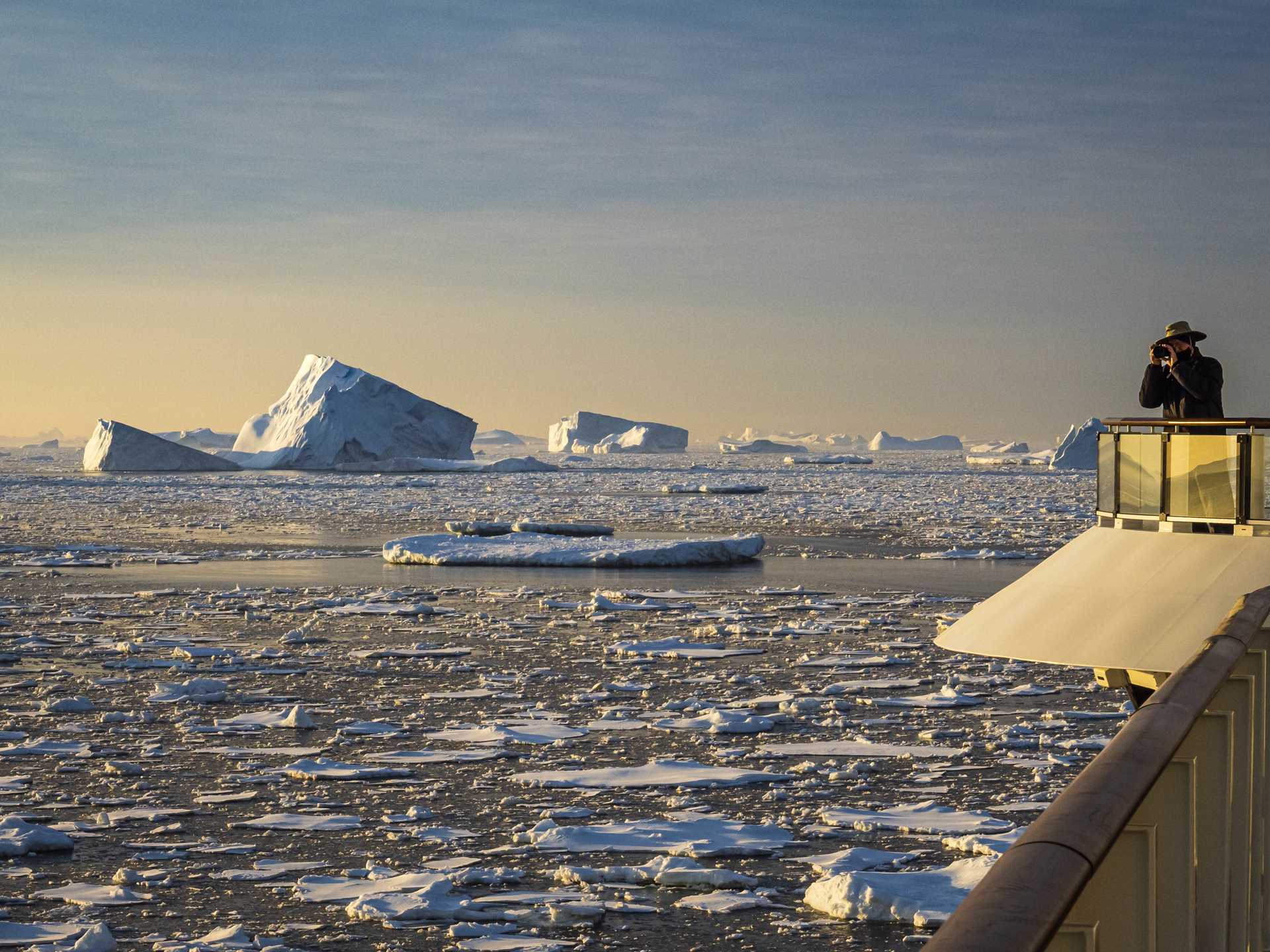 A guest photographs the Antarctic sunrise from the deck of the National Geographic Resolution with melting ice pack in the water.